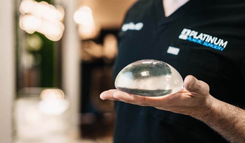 Dr. Costa holding a silicon breast implant in his hand.